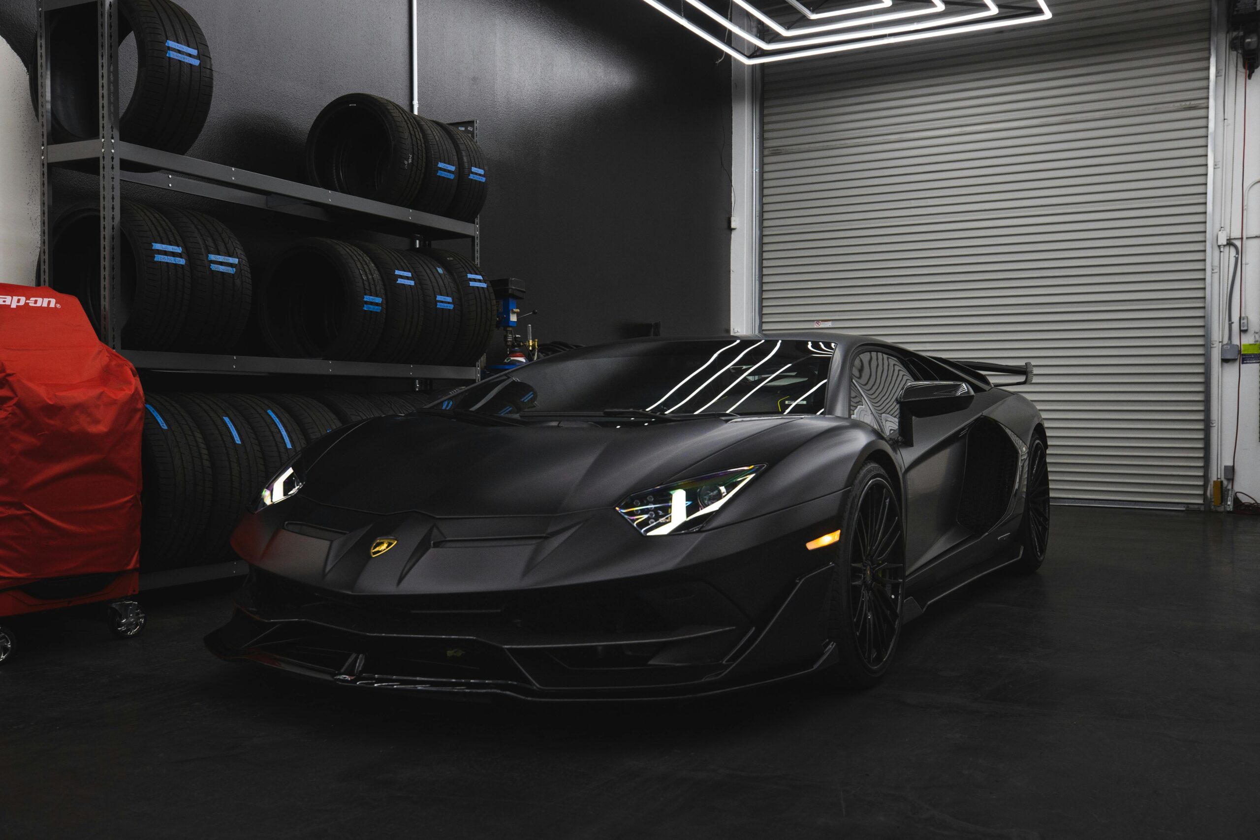 Luxury black Lamborghini in a contemporary garage setting with wheels and tools.